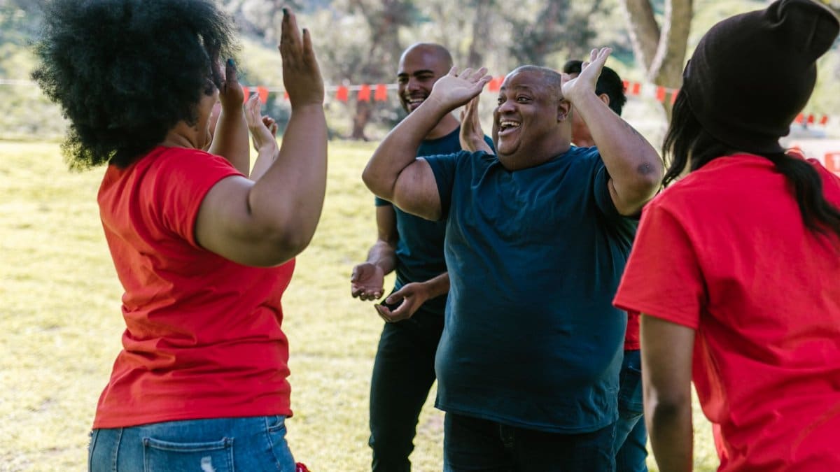 A joyful group of diverse adults high-fiving each other outdoors, showcasing team spirit.