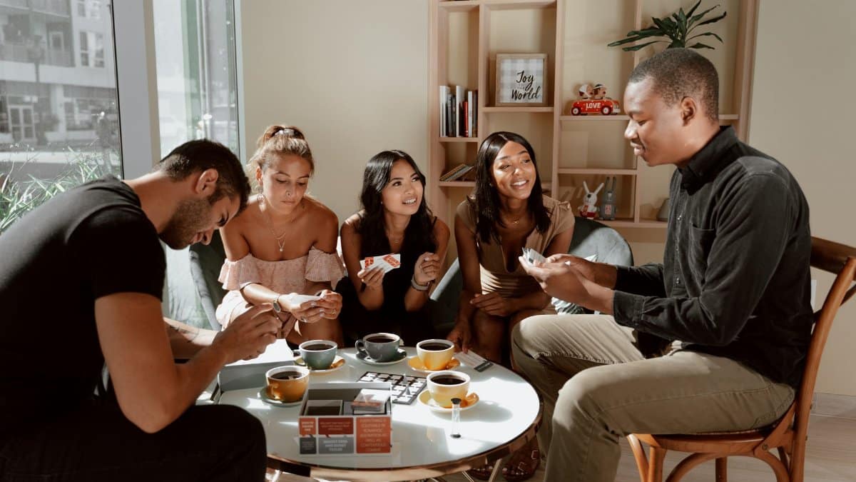 Group of diverse friends playing board games in a cozy café setting, enjoying coffee together.