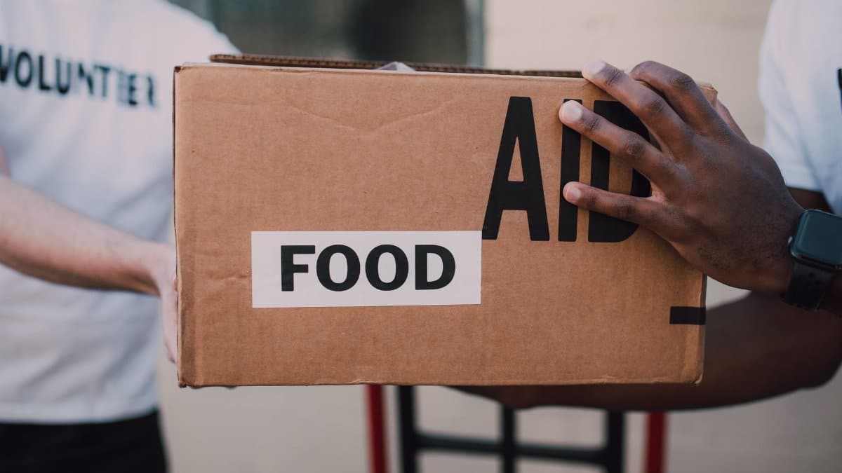 Two volunteers handing over a box labeled 'Food Aid', symbolizing community support.