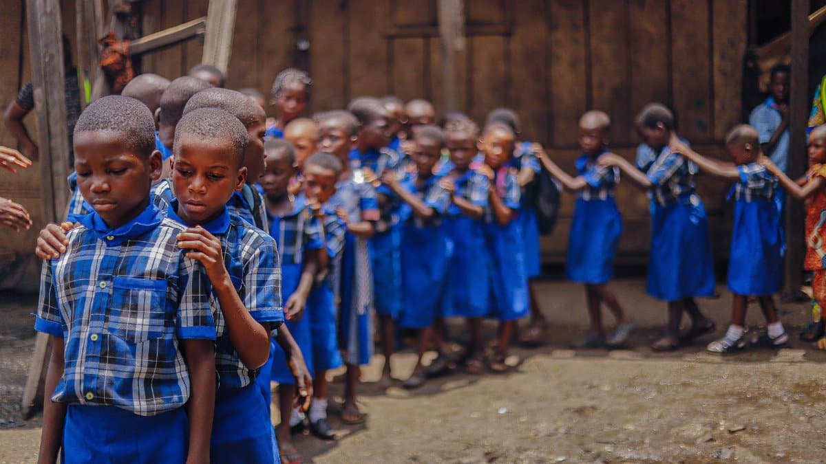 Group of school children in blue uniforms standing in a line outdoors.