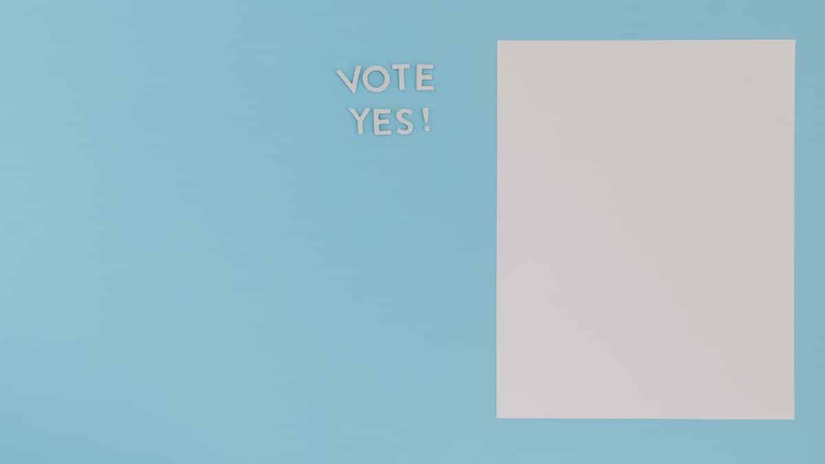 A minimalist concept image featuring 'Vote Yes' text and blank paper on a blue background.