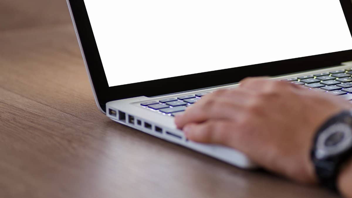 Close-up of a hand using a laptop with a blank screen, ideal for adding custom content.