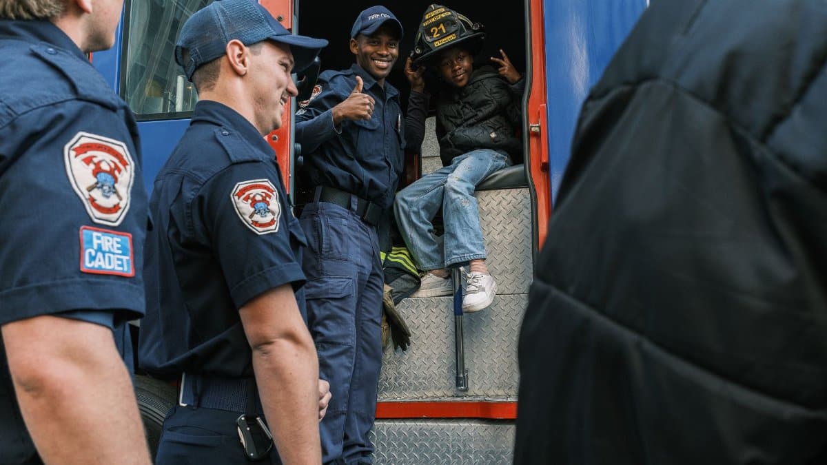 Firefighters interact with a child on a fire truck, fostering community spirit in an outdoor setting.