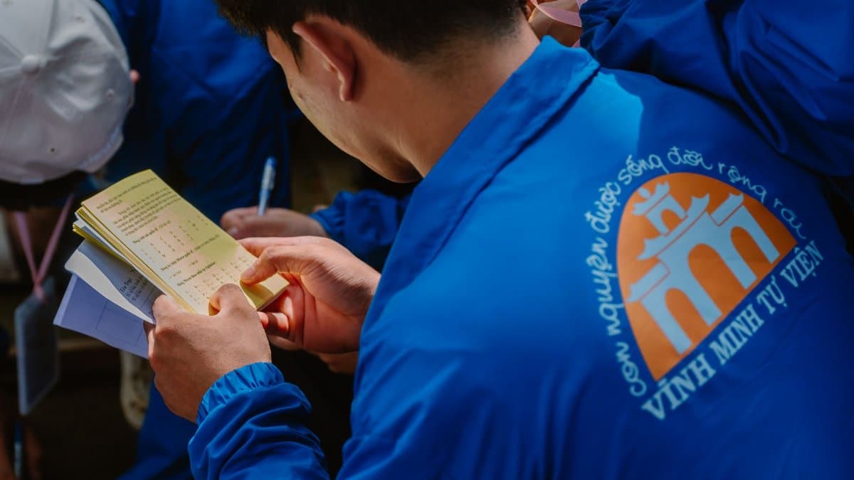 A volunteer reads a booklet at a community gathering, captured candidly in a lively setting.