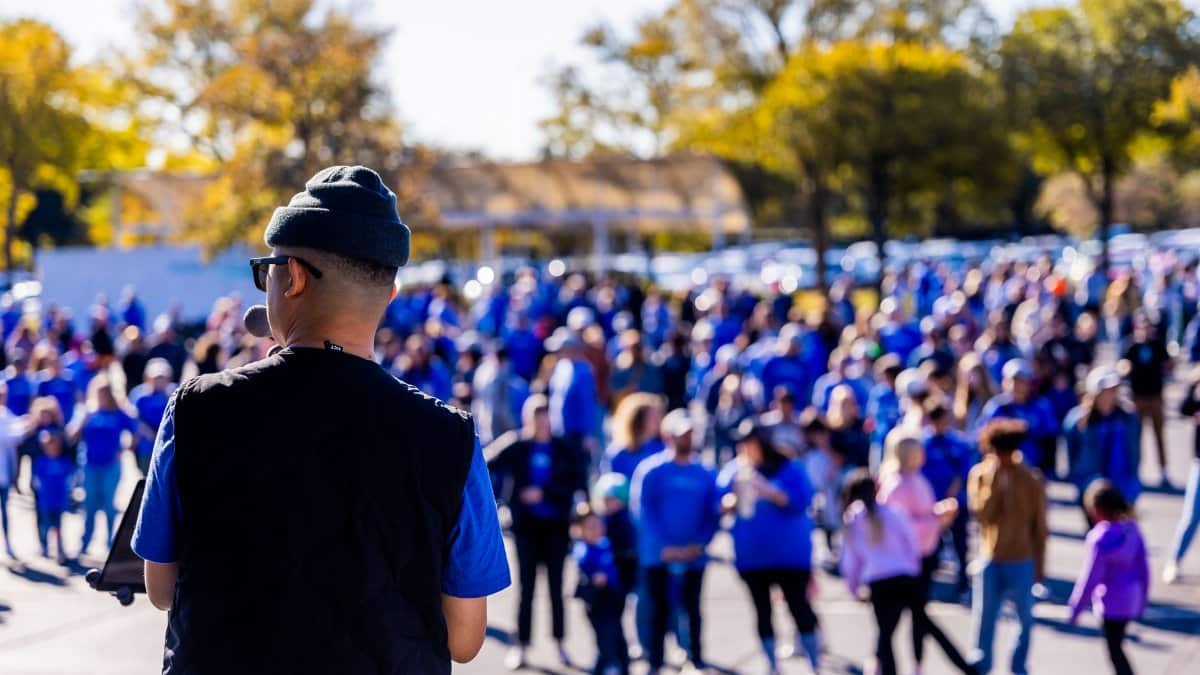 A speaker addresses a large crowd gathered outdoors, signifying a community event with a lively atmosphere.