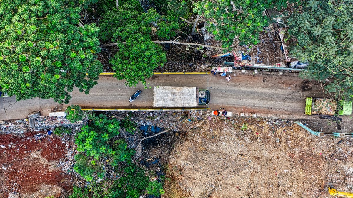 Aerial drone shot of a dirt road in South Tangerang, showcasing lush greenery and construction debris.