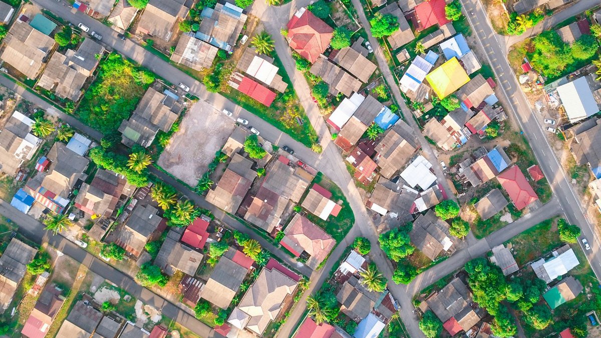Drone view of small multi colored private houses and verdant trees surrounded by long narrow roads in daylight in summertime