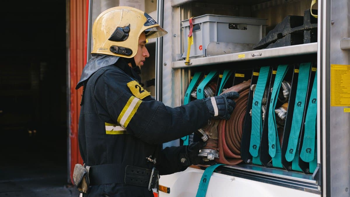 A firefighter in full gear organizes hoses in a fire truck, demonstrating safety and preparedness.