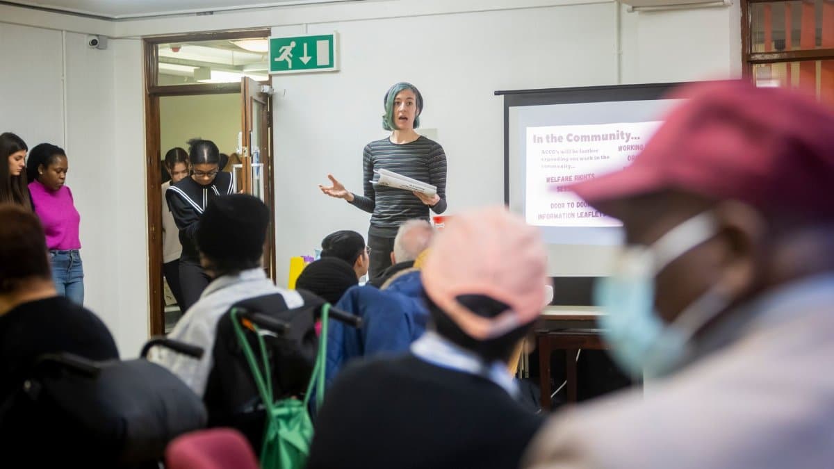 A diverse group attending a community meeting with a presenter speaking in front of a screen.