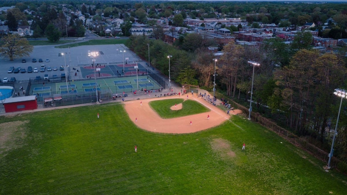 Aerial shot of a baseball game in a Philadelphia park at dusk, capturing sports action and community life.