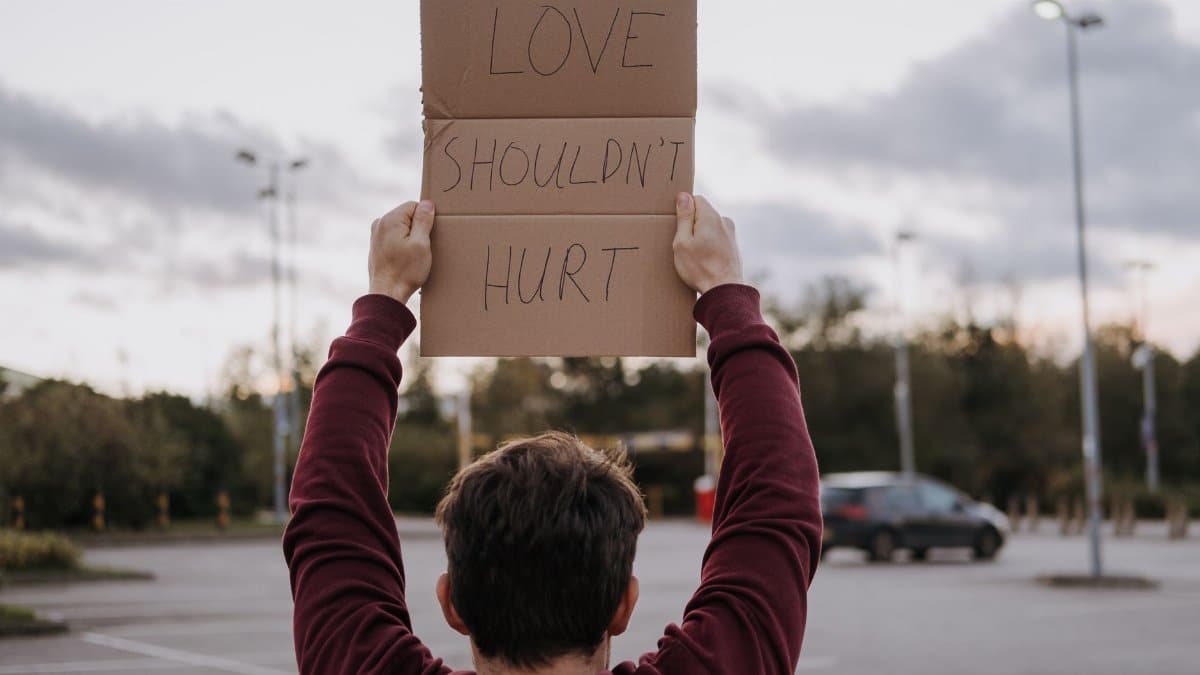 Back view of anonymous male with slogan love should not hurt on carton on street