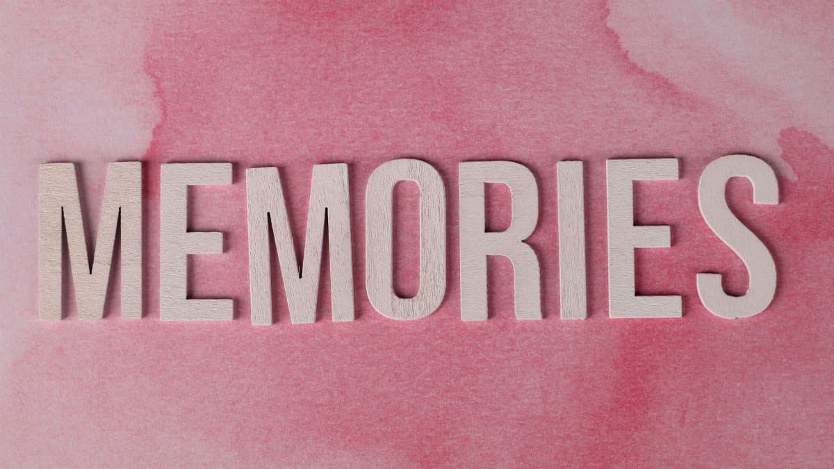 Wooden letters spelling 'Memories' on a pastel pink textured background.