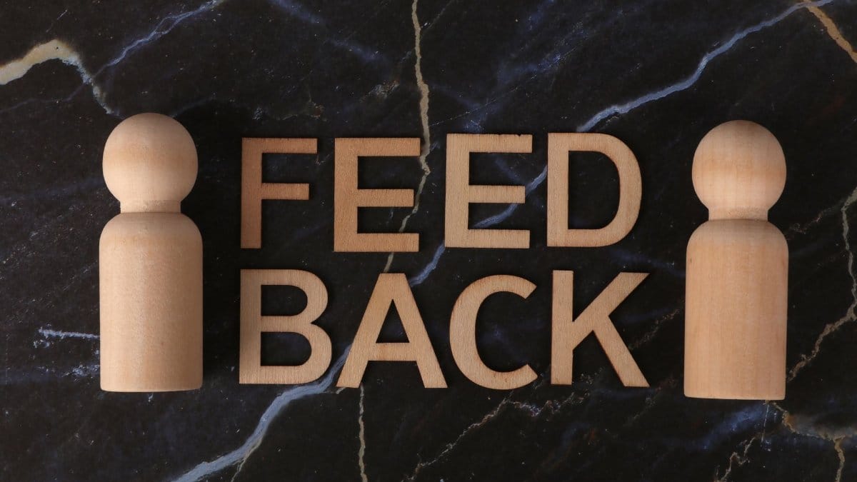 Wooden letters spelling 'Feedback' with peg-like figures on marble background.