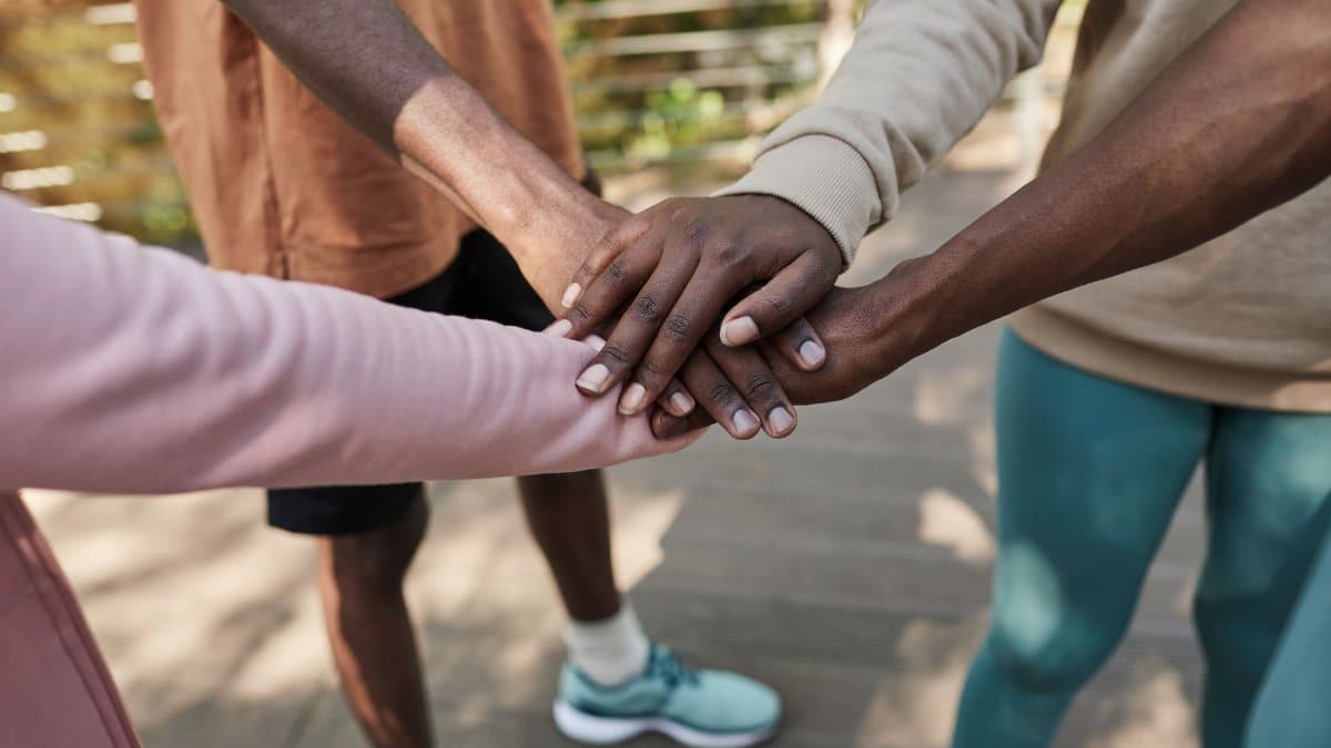 Diverse group showing teamwork and support with hands united. Outdoors setting.