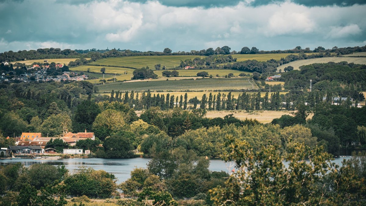 A beautiful countryside landscape near London featuring rolling hills and lush greenery under a dynamic sky.