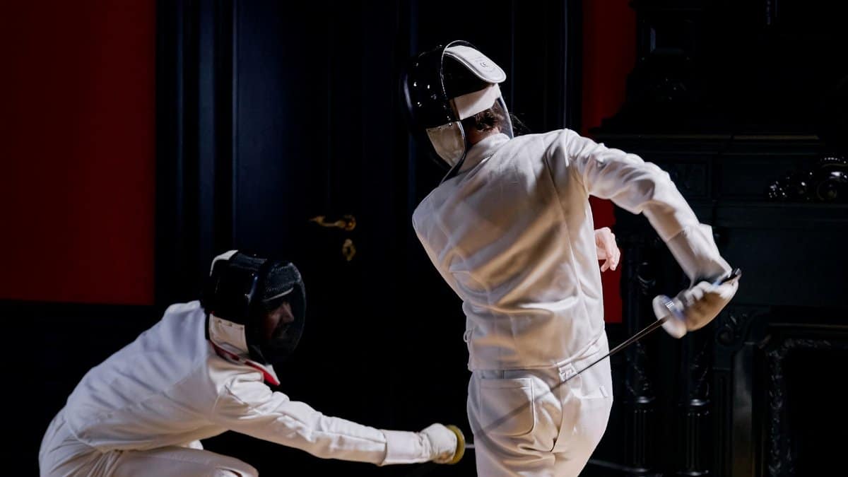Two fencers engaged in an intense indoor fencing duel, showcasing skill and agility.