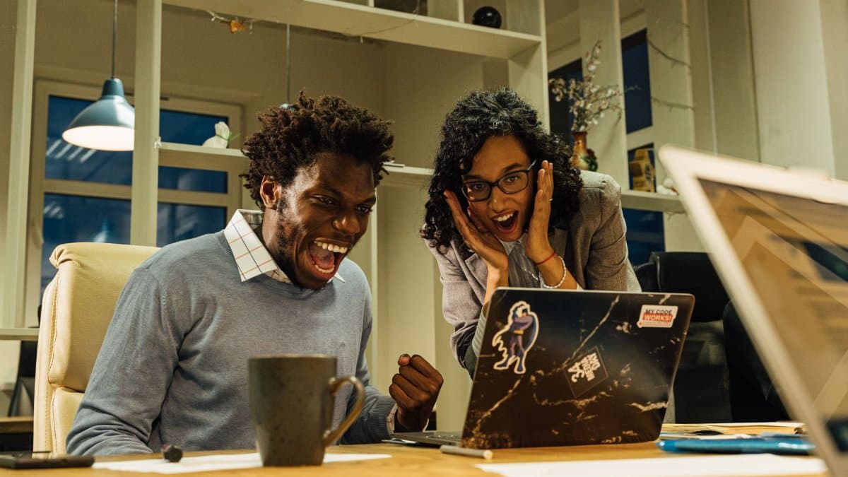 Excited colleagues celebrate a success on a laptop screen in a vibrant office setting.