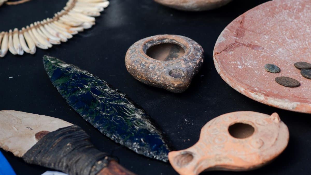 A curated display of ancient artifacts including pottery, tools, and ornaments on a black surface.