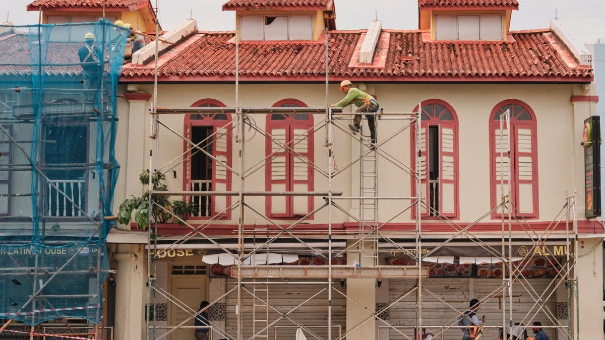 Workers on scaffolding renovating a historic building facade with red roof and tall windows.
