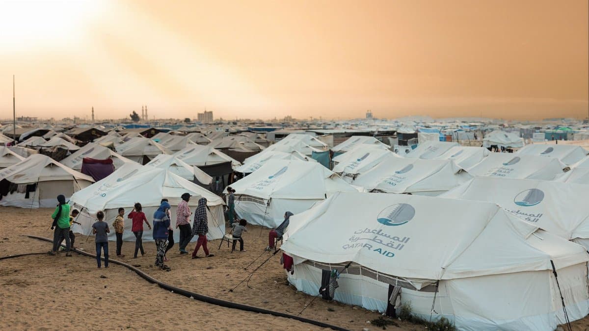 A crowded refugee camp with aid tents at sunset, highlighting human resilience.