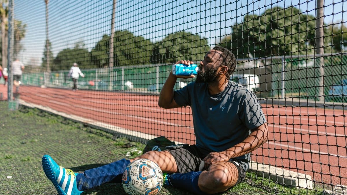 Soccer player resting by a field, hydrating after practice on a sunny day.