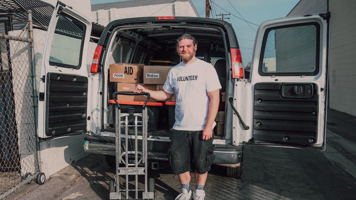 A volunteer unloads aid supplies from a van on a sunny day, showcasing community service efforts.