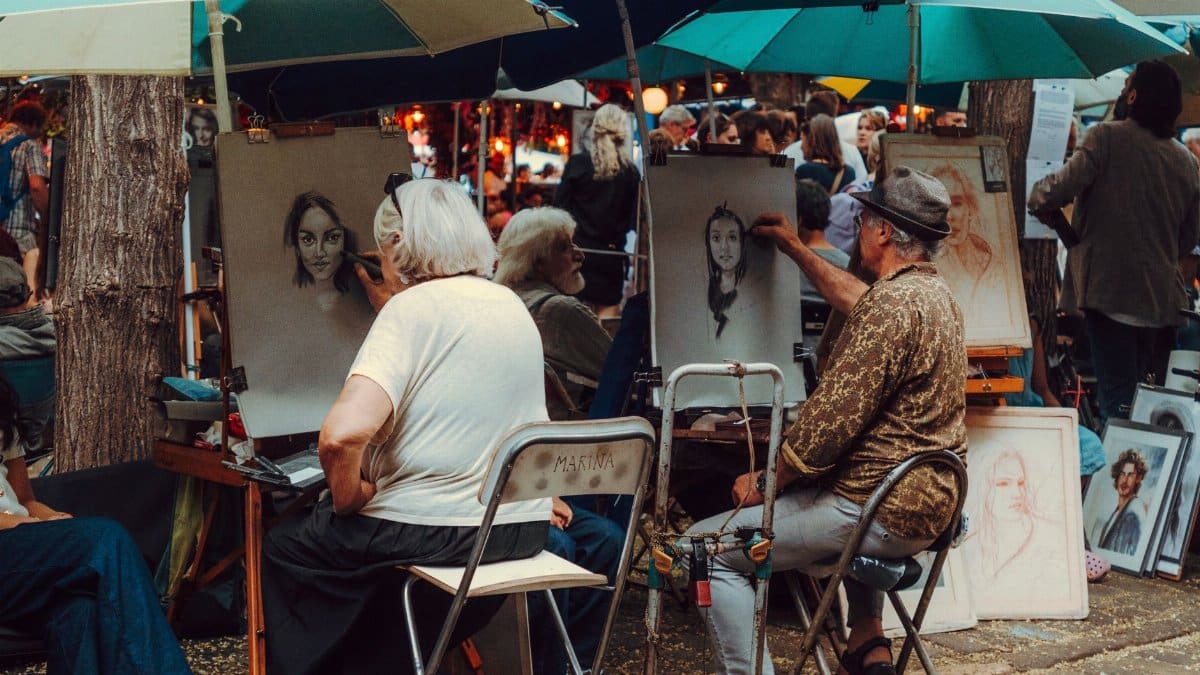 Street artists capture portraits in a lively outdoor market, showcasing artistic talent.