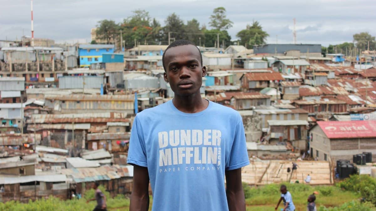A young man stands in front of Nairobi's Kibera slum, showcasing urban life and community spirit.