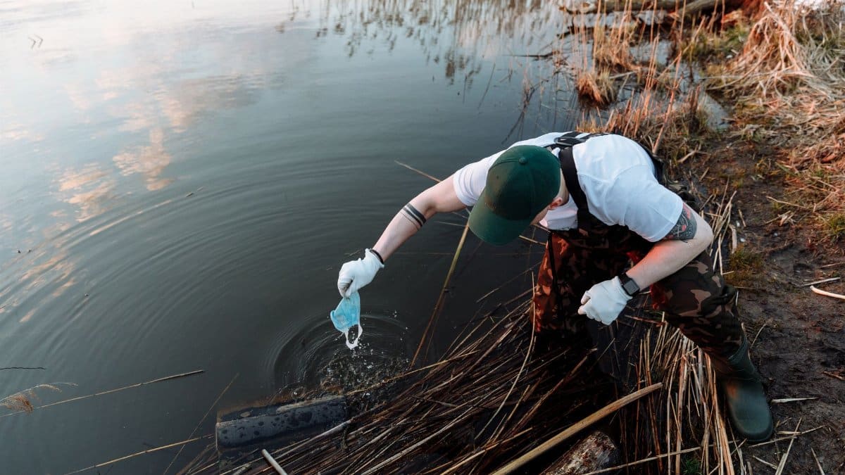 Volunteer collecting trash along a lake to promote environmental conservation.