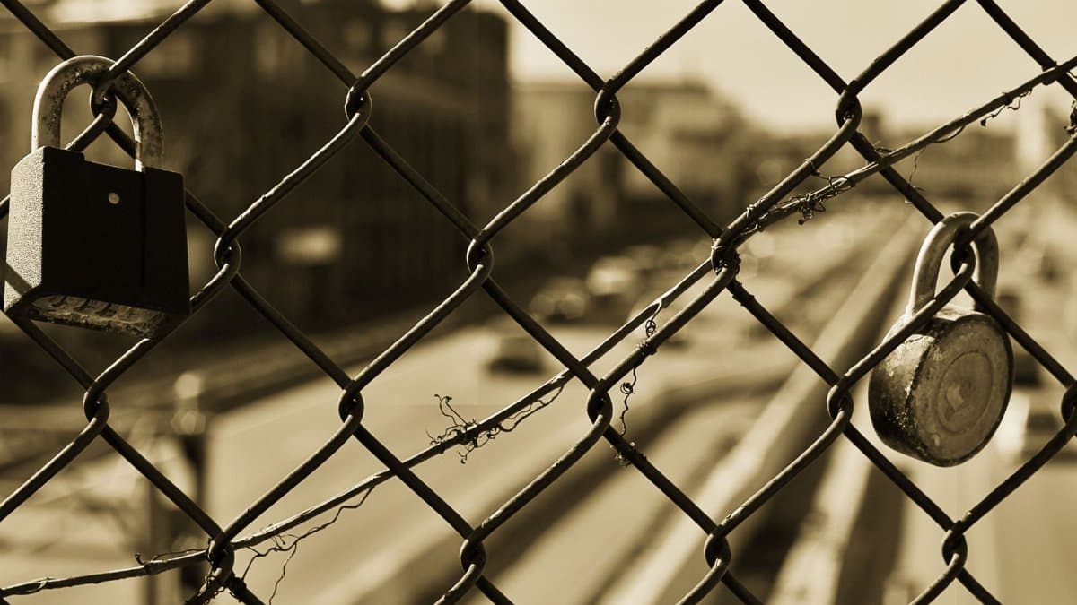 Sepia image of a chain link fence with two locks overlooking a blurred urban street.
