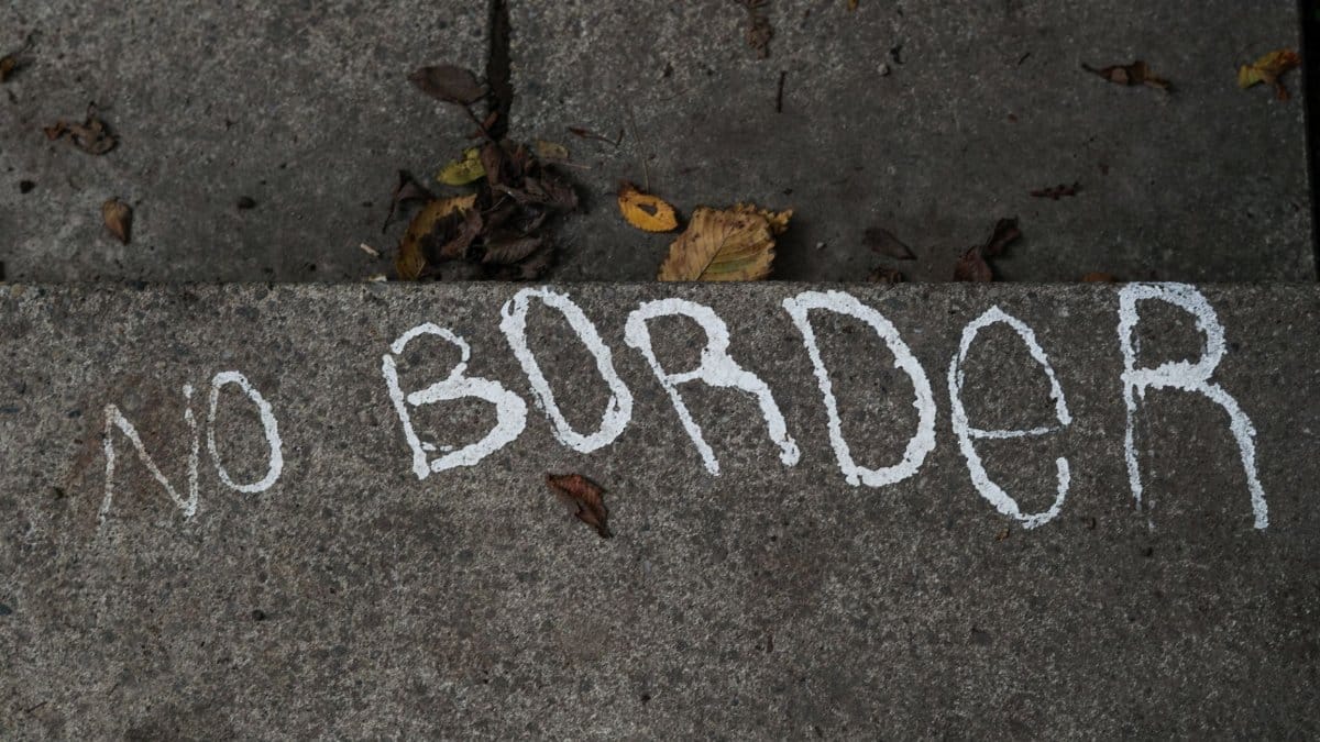 White text 'No Border' on a concrete surface surrounded by fallen leaves. Urban message on gritty pavement.