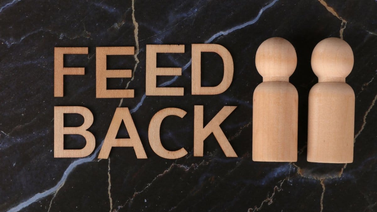 Wooden figures and 'feedback' text on black marble background, symbolizing communication and review.