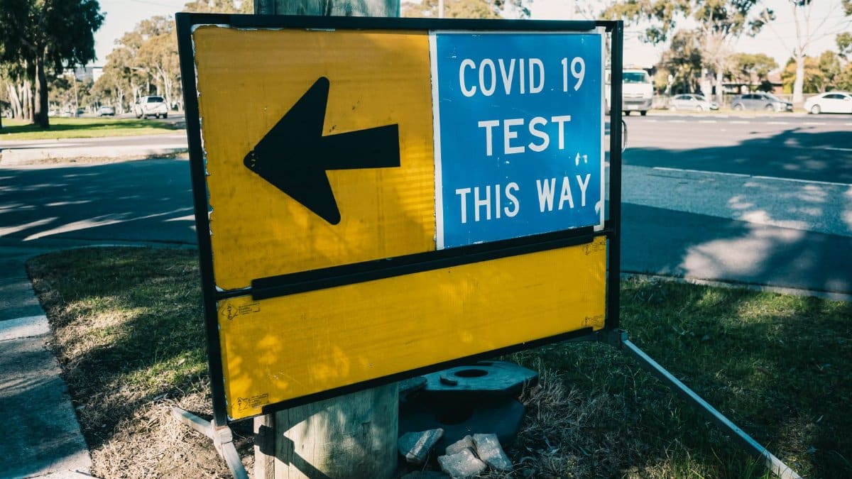 Outdoor view of a COVID-19 testing directional sign with an arrow pointing left.