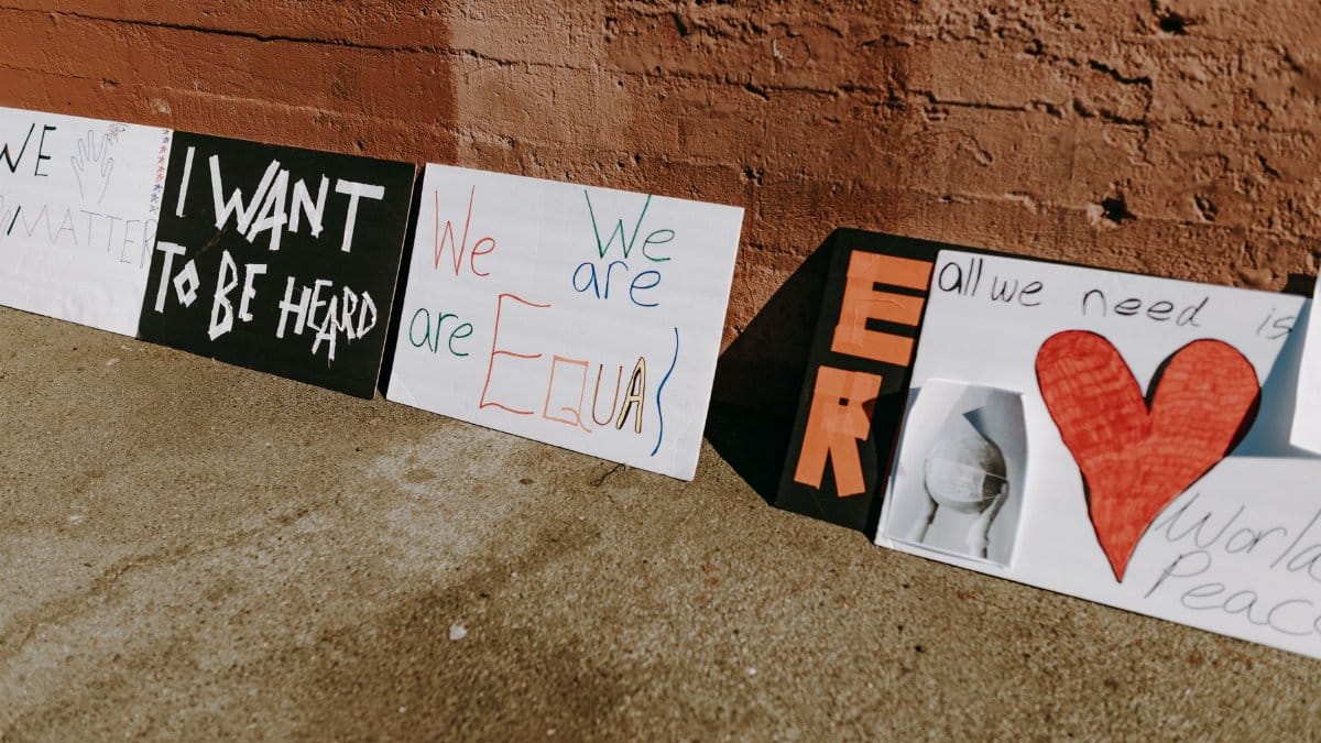 Outdoor protest signs advocating equality and peace placed against a wall.