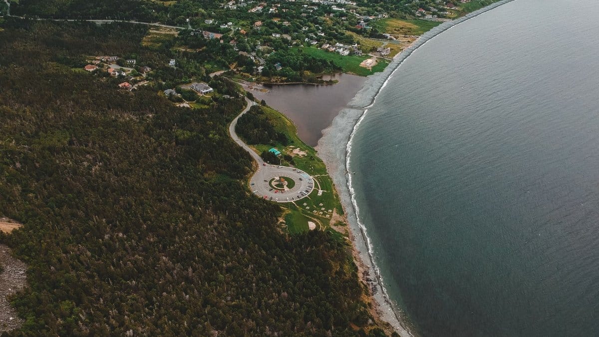 Drone shot of a scenic coastline with a circular plaza and forested area.
