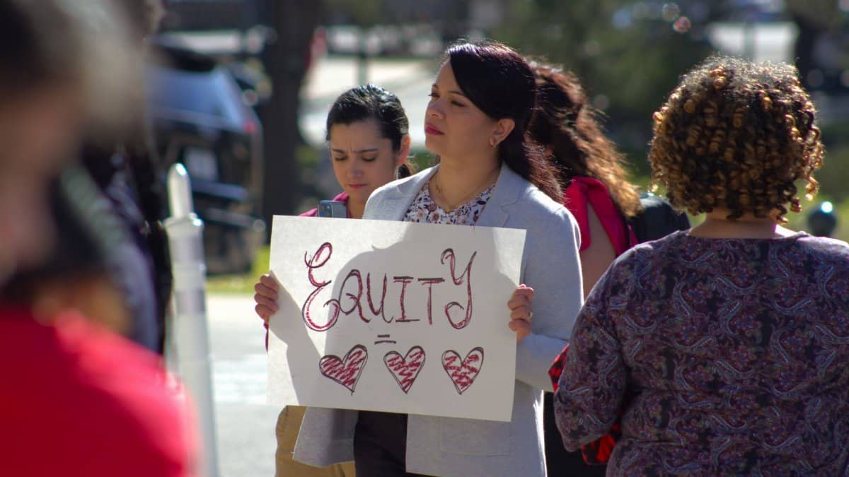 Women marching for equity holding signs in an outdoor protest in Austin, TX.