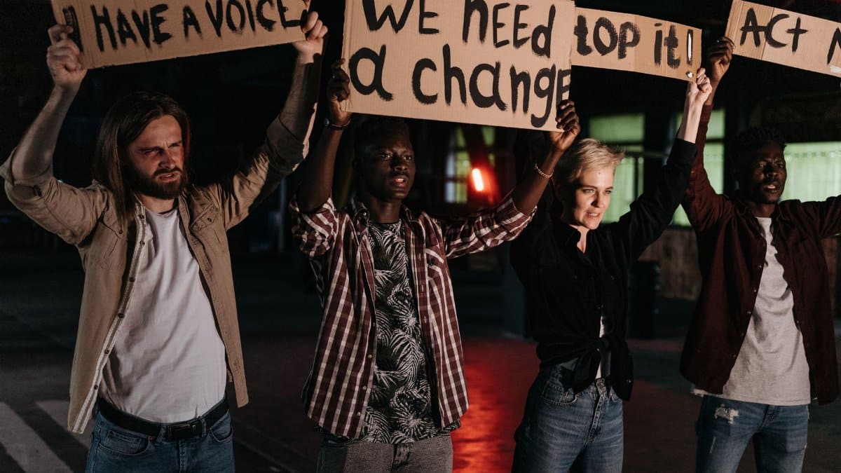 Diverse group holding protest signs demanding change, highlighted by night lighting.