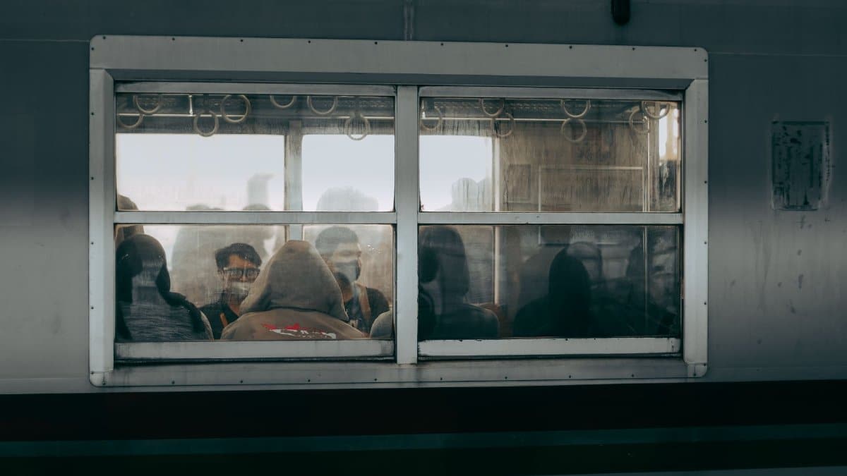 View of passengers inside a Jakarta commuter train, captured through a window, depicting daily city life.