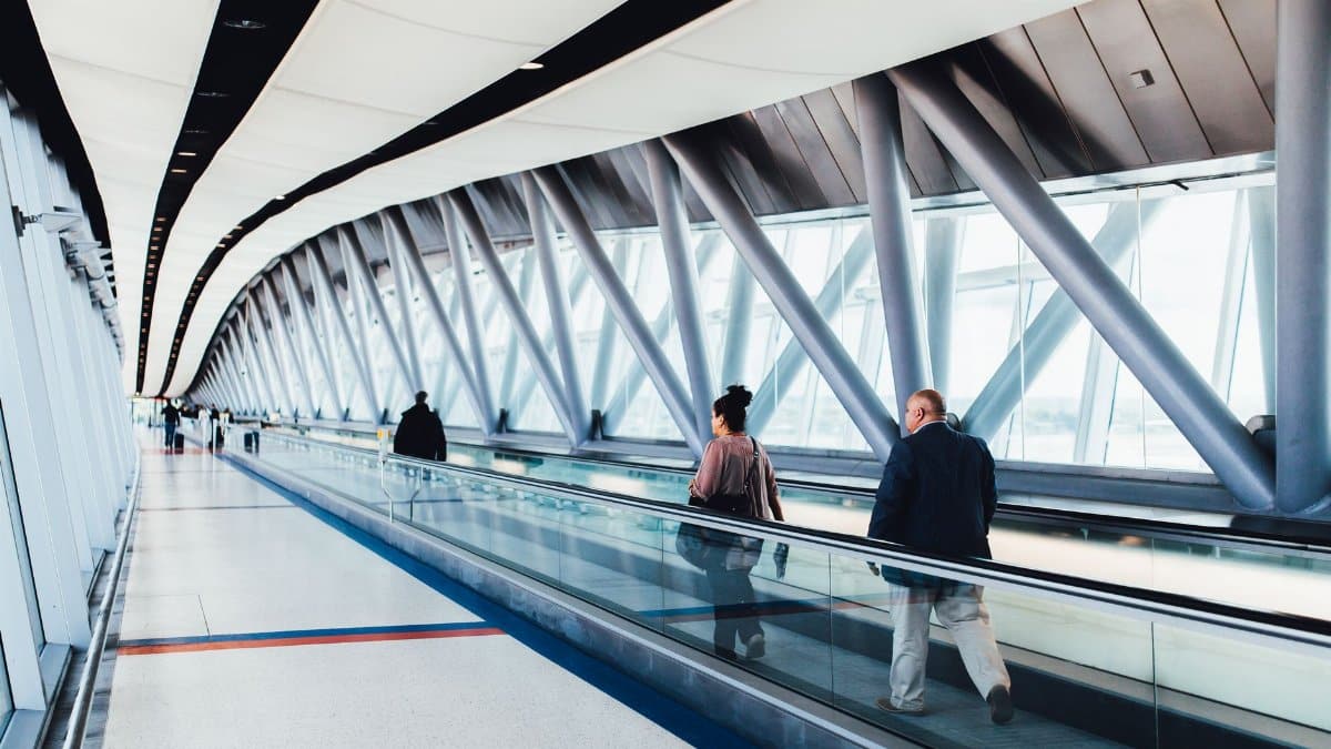 Travelers walking through a bright modern airport corridor with glass walls.