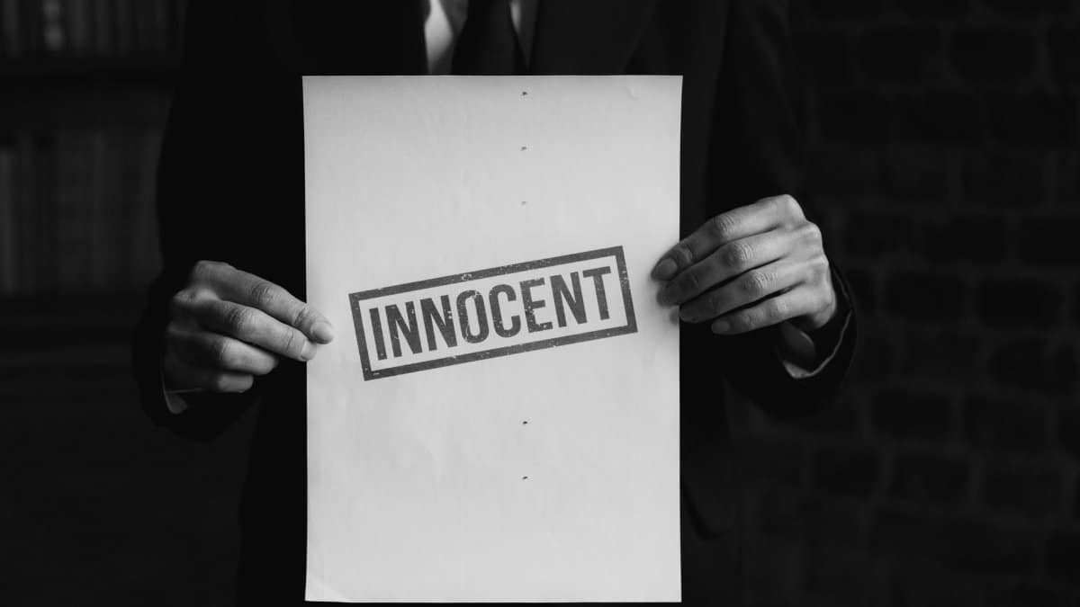A black and white photo of a person holding a paper with 'INNOCENT' text, conveying a message of legal or moral purity.