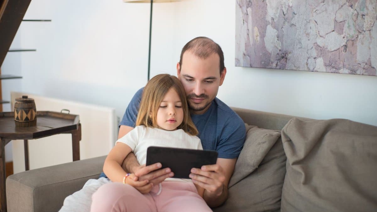 A father and daughter enjoying quality bonding time together on a couch using a tablet.