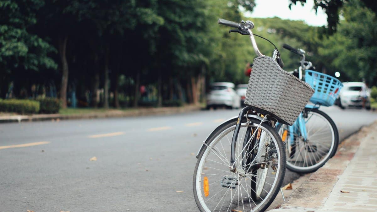 Two bicycles with baskets parked along a serene urban street, captured on a sunny day.