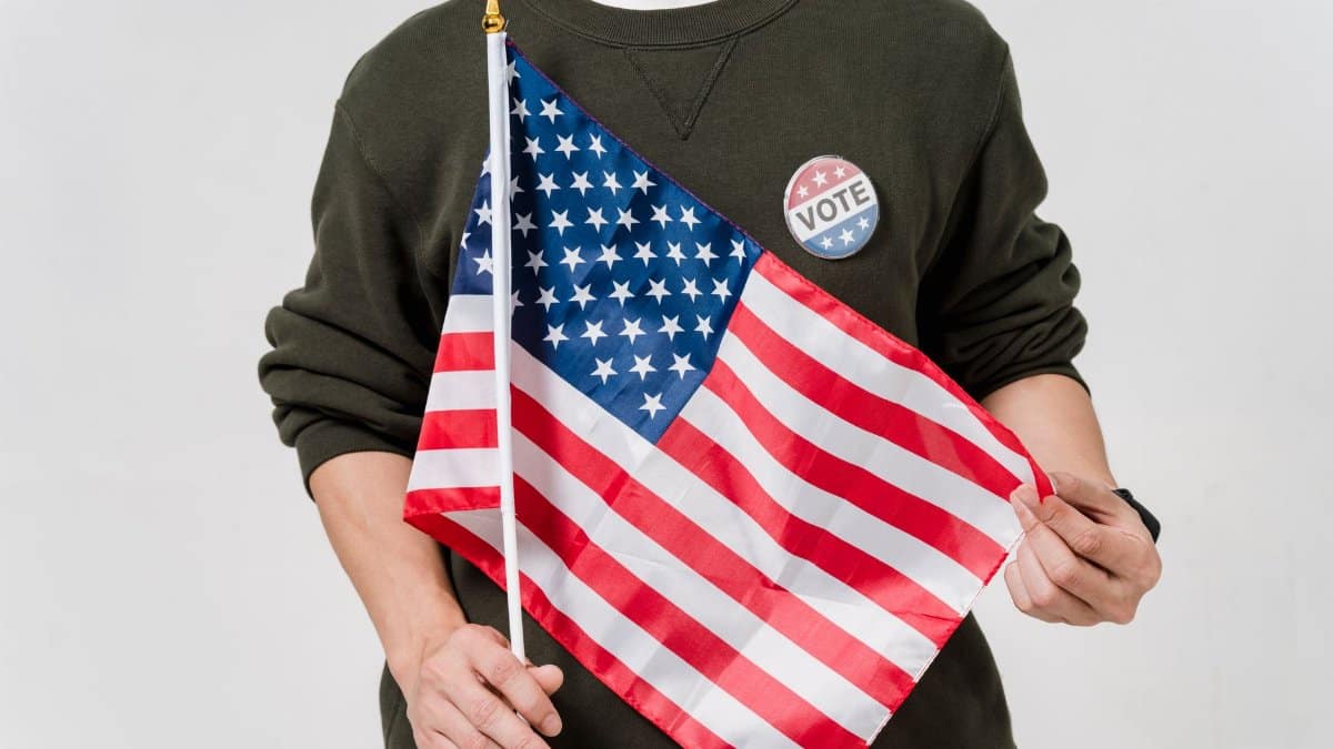 A man holding a USA flag and wearing a vote badge, symbolizing patriotism and democratic participation.