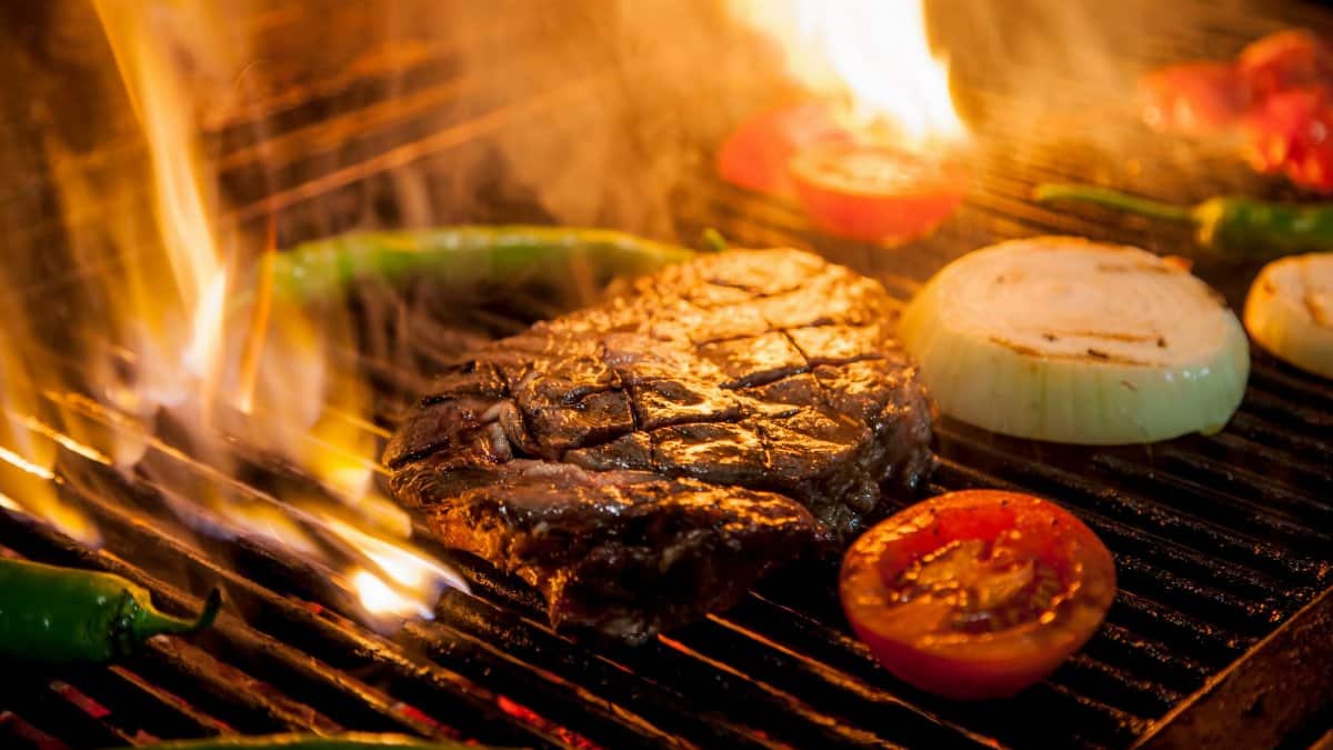 Flame-grilled steak with onions and tomatoes on a barbecue grill, ready to savor.