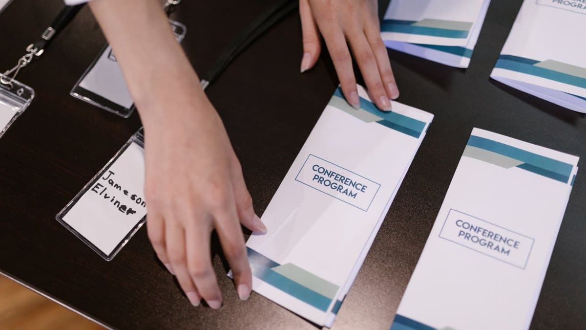 Hands organizing conference programs and name tags at event registration desk.
