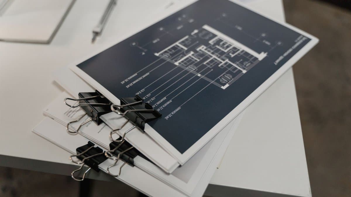Stack of architectural floor plans bound with clips on a white table, ideal for design projects.