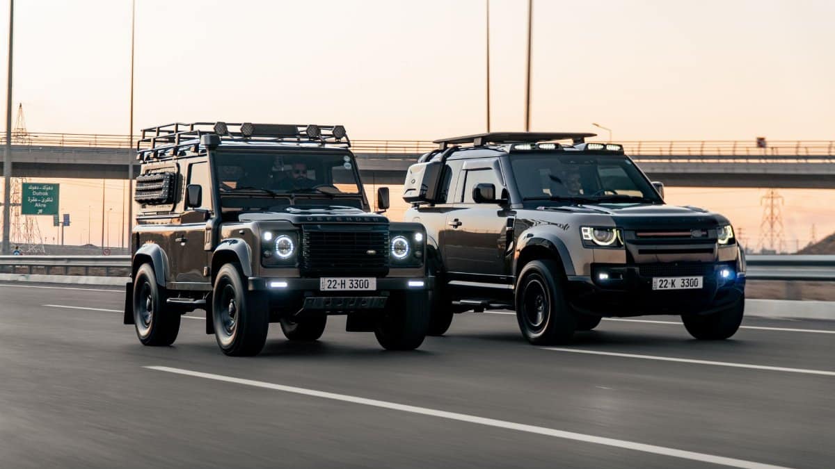 Two Land Rover Defenders driving side-by-side on a city highway in Erbil, Kurdistan at sunset.