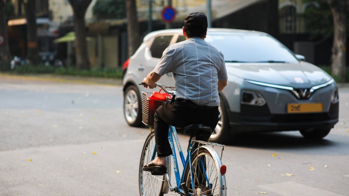 Man cycling on urban road with car nearby, showcasing busy city life.