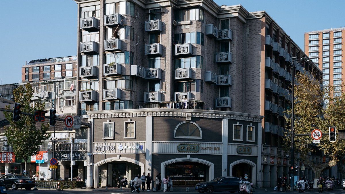 Street view of a multi-story apartment building with balconies at a bustling city intersection.