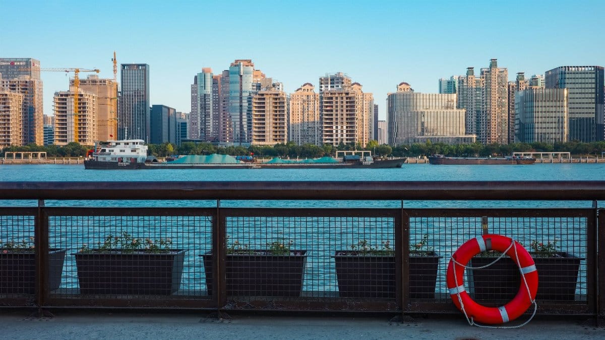 Scenic cityscape with modern buildings across the river, a life buoy on the waterfront railings.